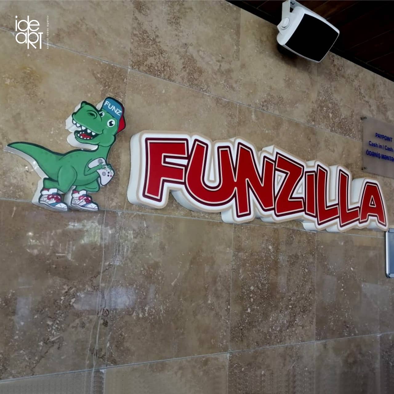 Daş divarda qırmızı Funzilla hərfləri və yaşıl dinozavr fiquru.