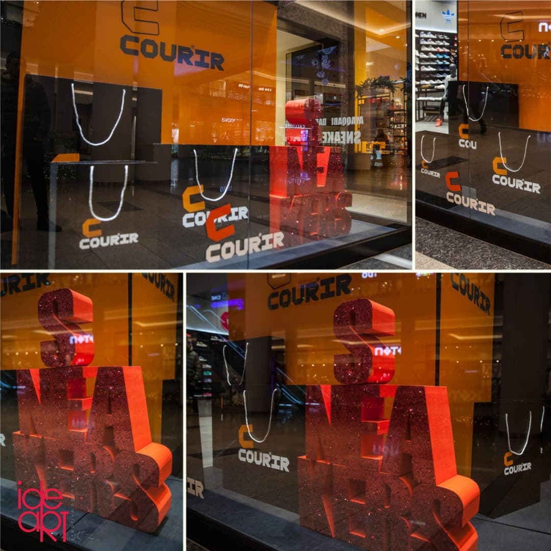 Courir window display featuring large dimensional letters and branded shopping bag props.